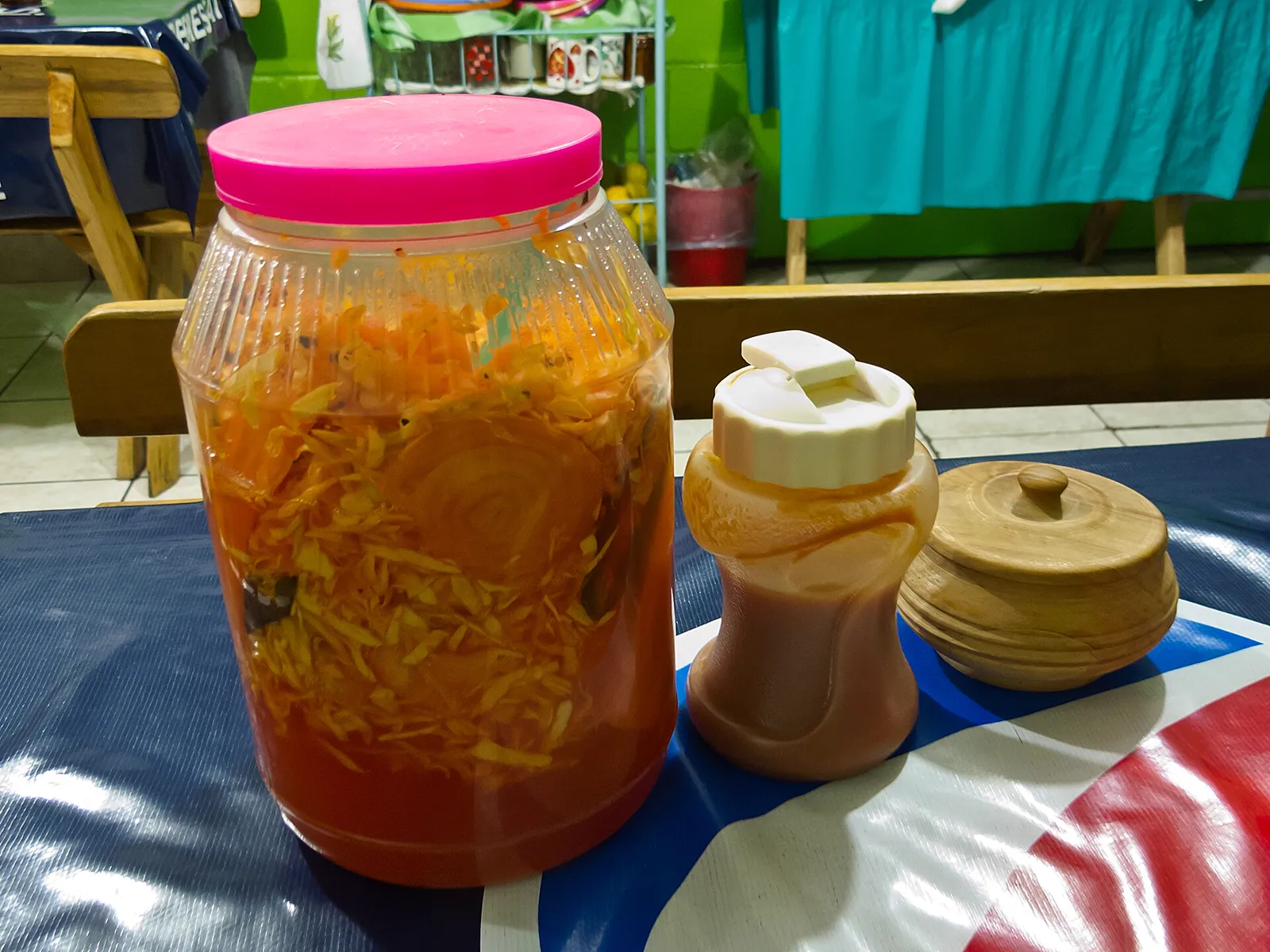 A jar of orange curtido with a tomato-sauce bottle