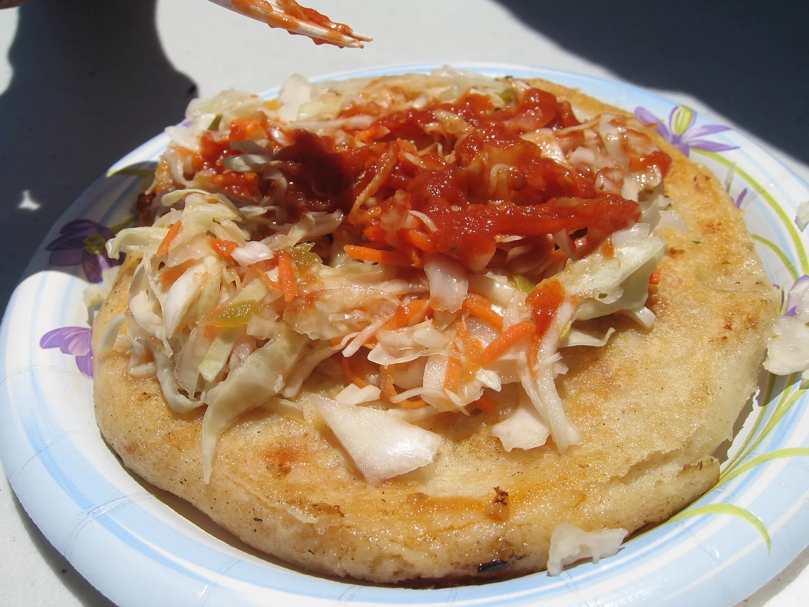 A pupusa topped with curtido and red salsa