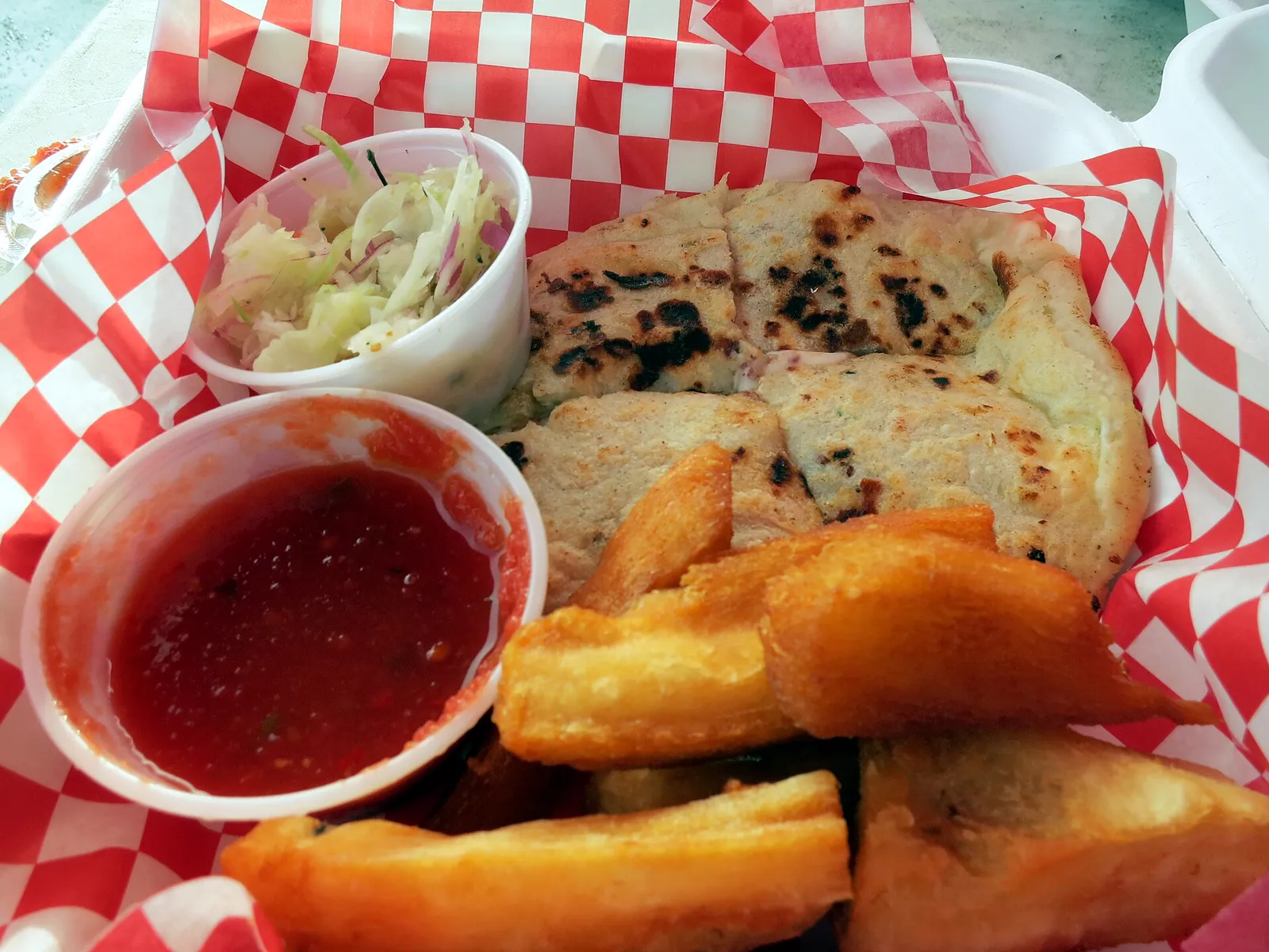 Pupusas with fried yuca and slaw in a red-checkered basket
