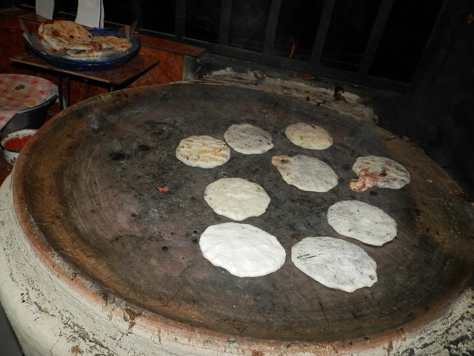 Seven pupusas cooking on a clay comal