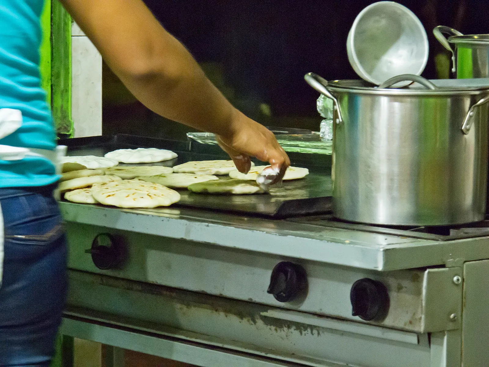 Hands turning pupusas on a griddle